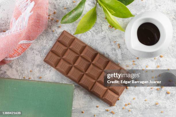 top view of a table with a bar of dark chocolate, accompanied by a book, a branch and a cup of coffee - candy samples ストックフォトと画像