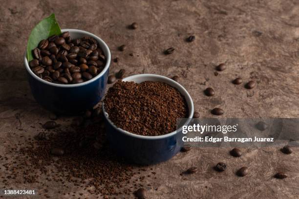 ground coffee and coffee beans in cups with a brown background. - grano cafe fotografías e imágenes de stock