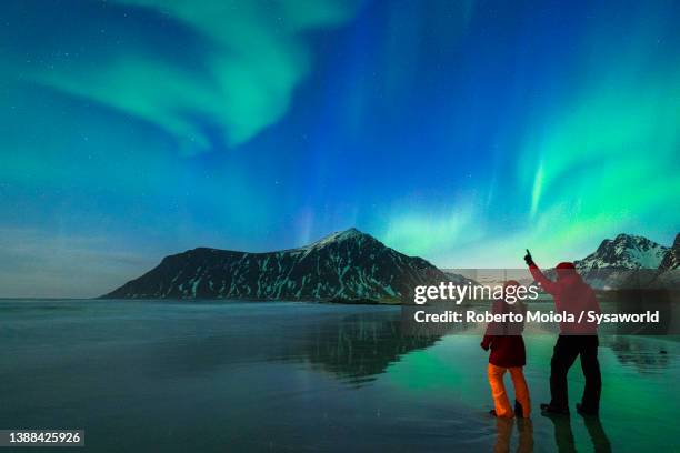 man and woman watching northern lights from skagsanden beach - aurora borealis stock-fotos und bilder