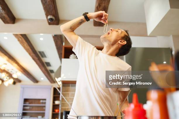 man trying pasta and cooking lunch at home - chef smelling food stockfoto's en -beelden
