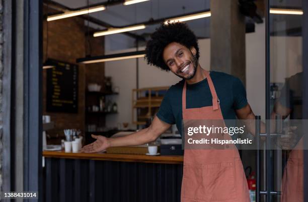 feliz camarero abriendo la puerta de una cafetería y dando la bienvenida a los clientes - brazil open fotografías e imágenes de stock