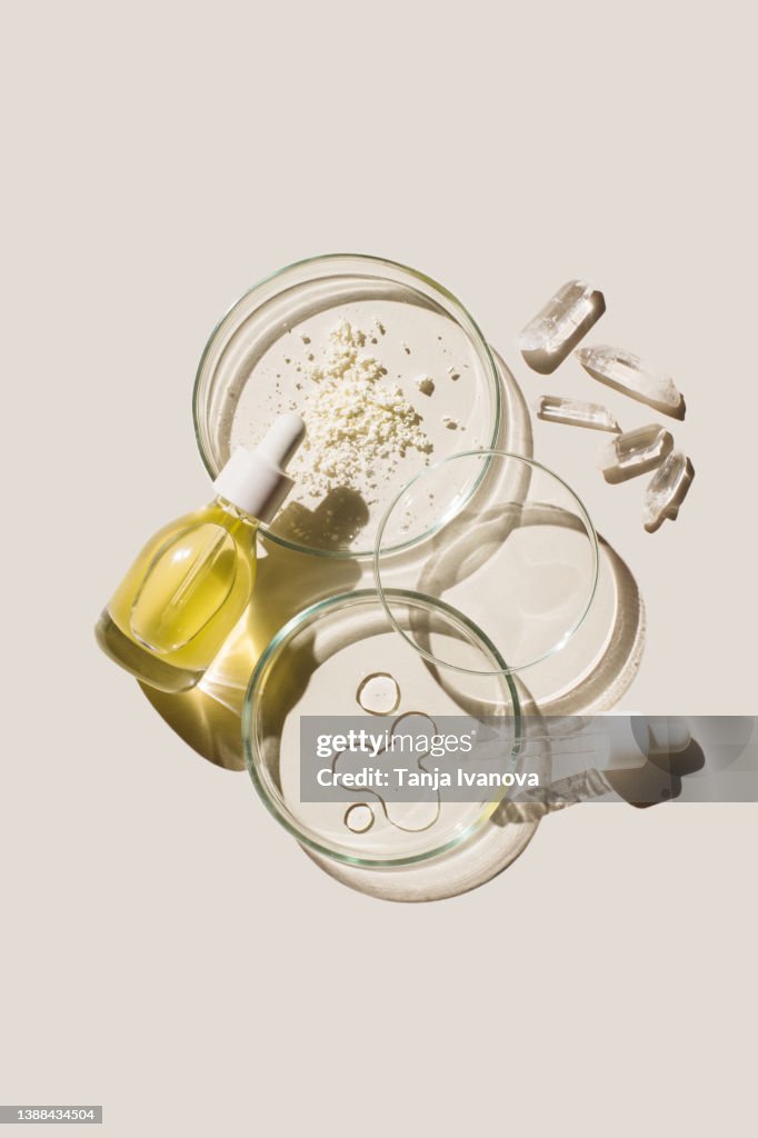 Petri dishes with sample beauty products and cosmetic glass bottle on beige background. Concept of laboratory research of cosmetics. Dermatology science. Natural medicine, cosmetic research, organic beauty products. Top view, flat lay.