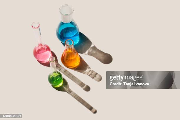 laboratory glassware with multicolored liquids on beige background. natural medicine, cosmetic research, bioscience, organic skin care products. top view, flat lay, copy space. - glass beaker stock pictures, royalty-free photos & images