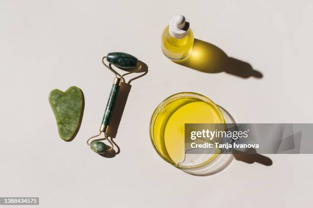 cosmetic glass bottle with pipette, petri dish and jade face roller, guasha on beige background. skincare beauty product. flat lay, top view - 玉石滾輪 個照片及圖片檔