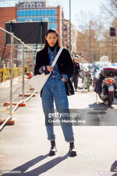 Chinese model Luoyi wears a black jacket, denim jumpsuit, black boots, and white leather cross-body bag after the Jil Sander show during the Milan...