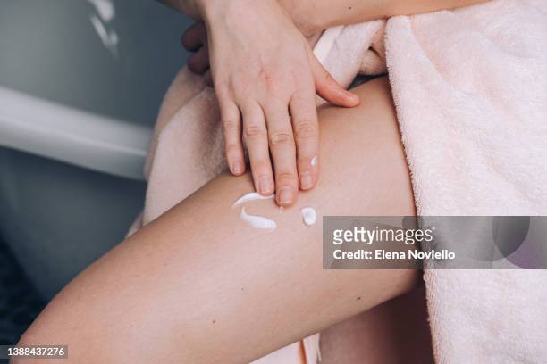 woman applies moisturizing lotion to her thigh skin,  body cream after showering - cellulite foto e immagini stock