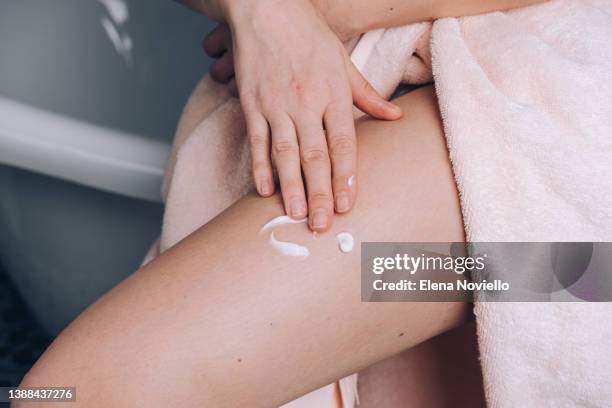 woman applies moisturizing lotion to her thigh skin, body cream after showering - hamstring stock pictures, royalty-free photos & images