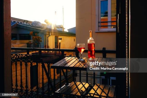 a bottle and a glass of wine on the table at the balcony of an old house at sunset. - sunlight through drink glass foto e immagini stock
