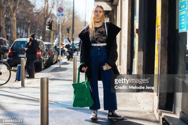 Model Ashton Day wears a black jacket, black necklace, black lace top, high-rise blue jeans, black Converse sneakers, and carries a green tote bag...