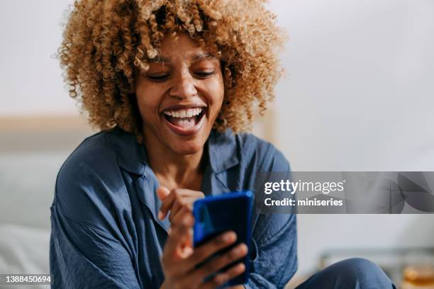 mujer sonriente usando el teléfono móvil en el dormitorio - reírse mujer fotografías e imágenes de stock