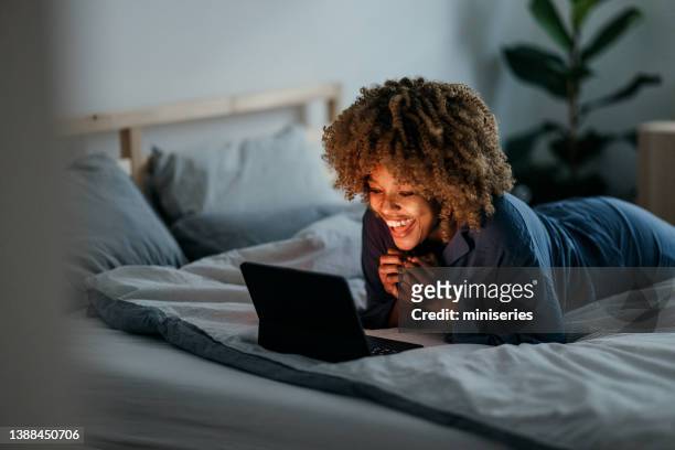 happy woman using digital tablet in her bedroom - african american woman pajamas residential building stock pictures, royalty-free photos & images