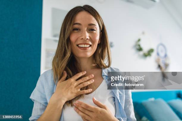 young woman holding hands on chest and smiling at camera as if she is on a video call - hands on chest stock pictures, royalty-free photos & images