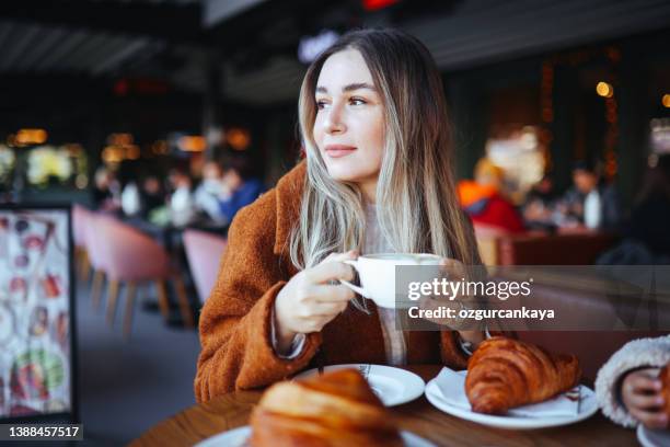 cappuccino and frensh croissant in the cafe. a woman eats her breakfast. - cappuccino and croissant stock pictures, royalty-free photos & images
