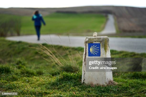 rear view of an adult woman walking with a camino de santiago cairn in the foreground. - steinpyramide stock-fotos und bilder