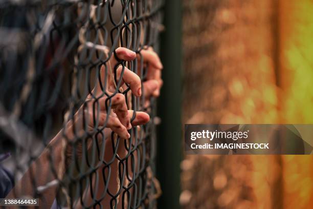 unrecognizable person clinging to a fence deprived of freedom - refugiado imagens e fotografias de stock
