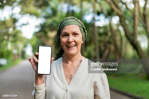 frau mit krebs hält smartphone - mature woman screen stock-fotos und bilder