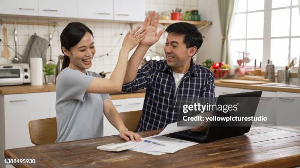 excited asian spouses reading paper letter with good news in the dining room at home. they give high five and clap hands celebrating for getting tax refund - income tax bildbanksfoton och bilder