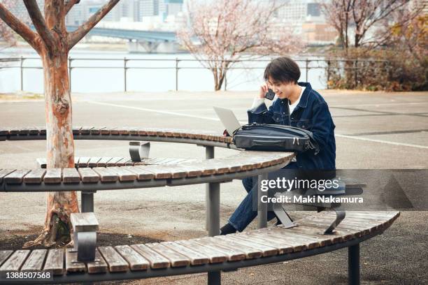 a man in his twenties working on a bench in a riverside park. - riverbank stock-fotos und bilder