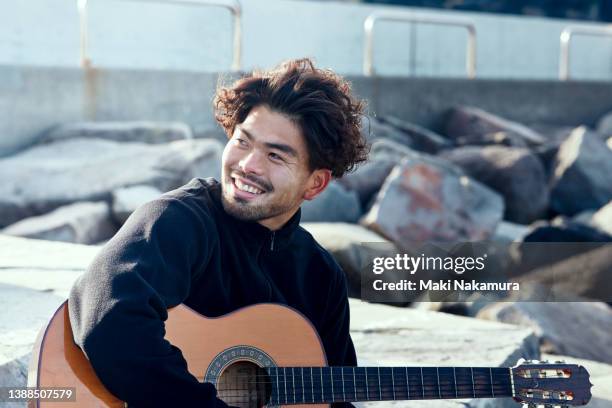 a young man playing the guitar on the rocks of the sea. - saiteninstrument stock-fotos und bilder