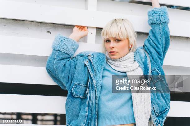 young blond short-haired woman in jeans clothes and a scarf standing and posing near white hut, outdoors - denim jacket mockup stock pictures, royalty-free photos & images
