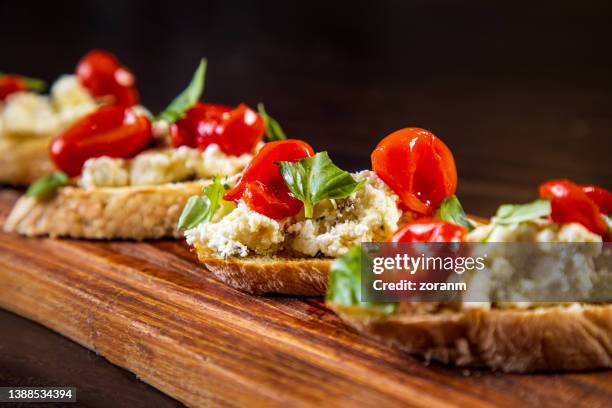 bruschetti con queso de cabra, tomate cherry y albahaca sobre tabla de madera - queso de cabra fotografías e imágenes de stock