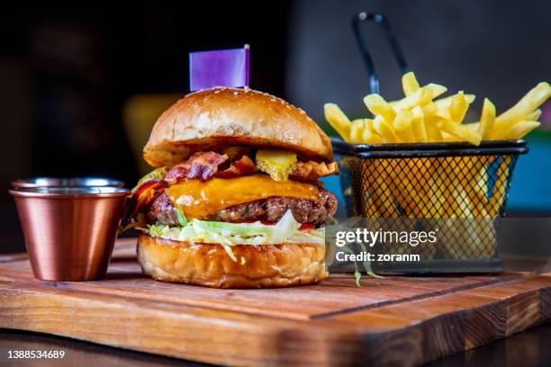 burger in bun with bacon slices and cheese, served with french fries - burger and fries stockfoto's en -beelden