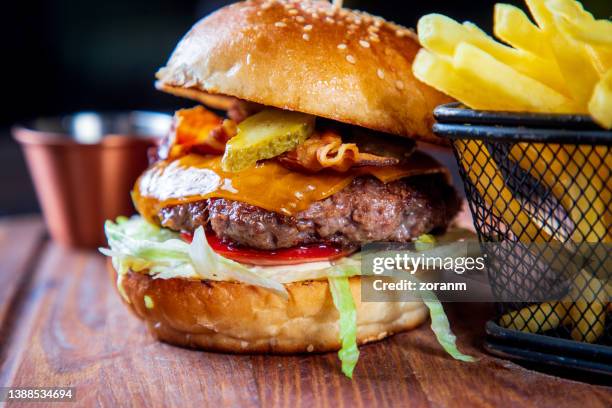 burger im brötchen mit speckscheiben und käse, serviert mit pommes frites, nahaufnahme - cheeseburger and fries stock-fotos und bilder