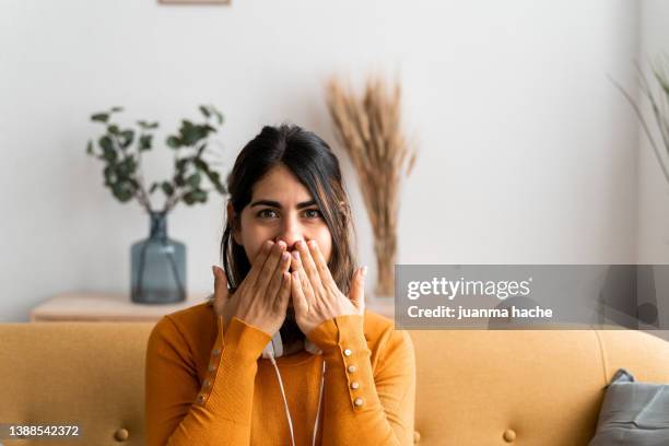 hispanic woman at home, with a surprised expression covering her mouth with her hands for making a mistake. - woman mouth stock-fotos und bilder