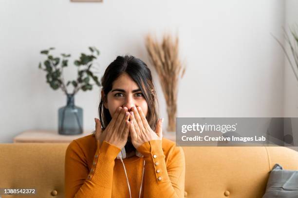 hispanic woman at home, with a surprised expression covering her mouth with her hands for making a mistake. - mano tapando la boca fotografías e imágenes de stock