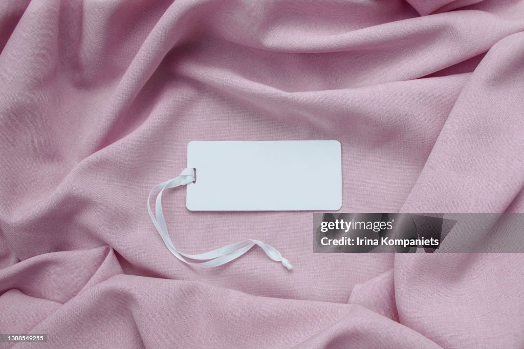 White empty paper label with a ribbon on a background of pink fabric close-up.