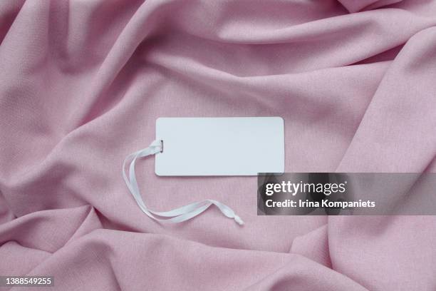 white empty paper label with a ribbon on a background of pink fabric close-up. - flatlay fashion stockfoto's en -beelden