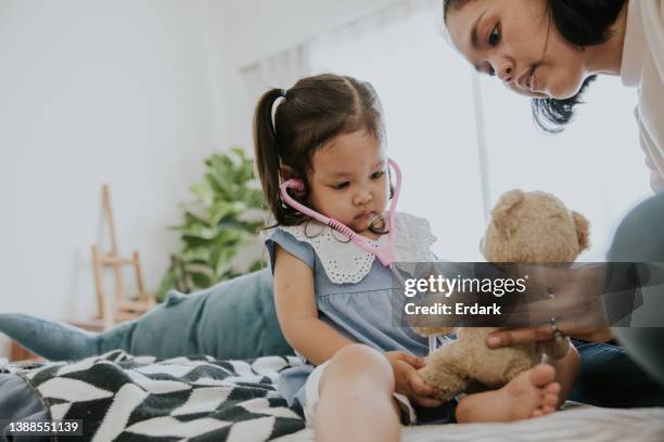 a garota segura estetoscópio imagina-se que é um médico ouvir o batimento cardíaco do ursinho de pelúcia. - mama bear - fotografias e filmes do acervo