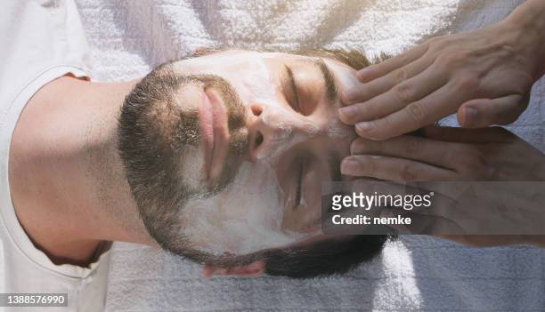 mann in maske auf dem gesicht im spa-schönheitssalon - hat on the head is worth stock-fotos und bilder