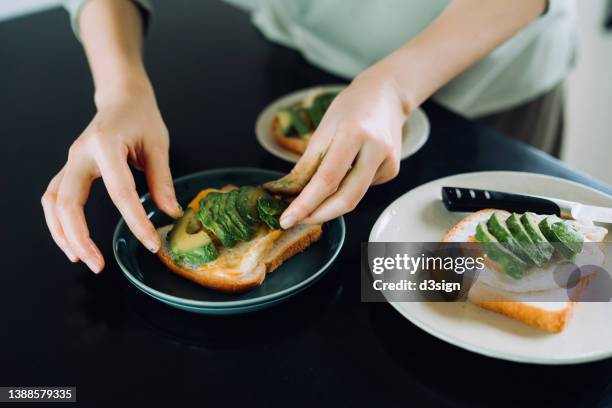 close up of young asian woman cutting avocado slices in the kitchen at home, preparing healthy breakfast with egg and avocado on toast in the morning. a healthy breakfast to start a great day ahead - 盛り付け 手 ストックフォトと画像