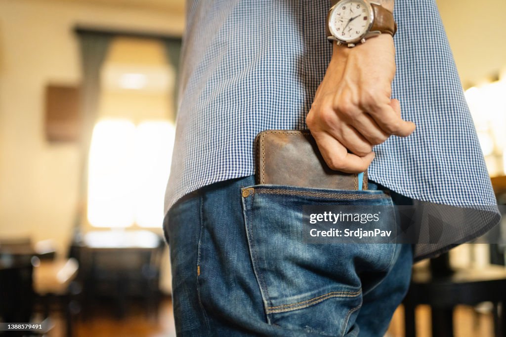 Un homme méconnaissable met son portefeuille en cuir dans la poche arrière du jean