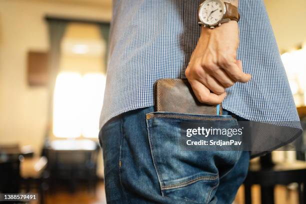 unrecognizable man puts his leather wallet into back pocket of the jeans - leather pants stockfoto's en -beelden