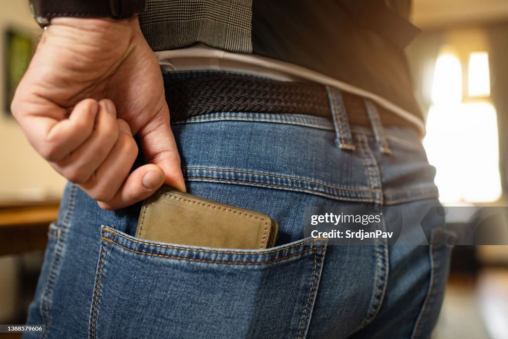Unkenntlicher Mann steckt sein Lederportemonnaie in die Gesäßtasche der Jeans