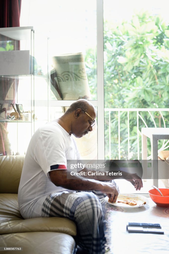 Senior Singaporean man eating roti prata at home