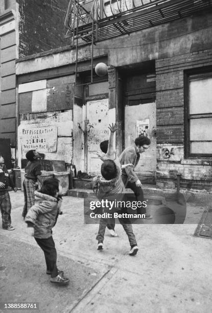 Pedestrian stoops out of the way of play as children play basketball, the two bottom rungs of the fire escape ladder are a good substitute for a...