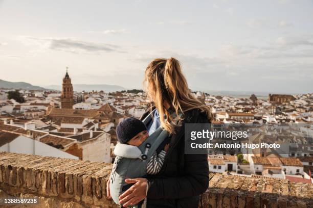 young woman sightseeing with her baby in a baby carrier. looking at the city of antequera from a viewpoint. - pure stock pictures, royalty-free photos & images