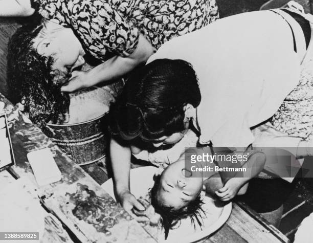 Young Japanese boy having his hair washed by his mother at the Santa Anita Assembly Center, on the grounds of the Santa Anita Park racetrack in...