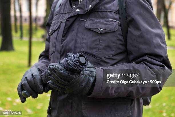 close-up of mans hand in jacket and gloves holding closed umbrella - water repellent stock pictures, royalty-free photos & images