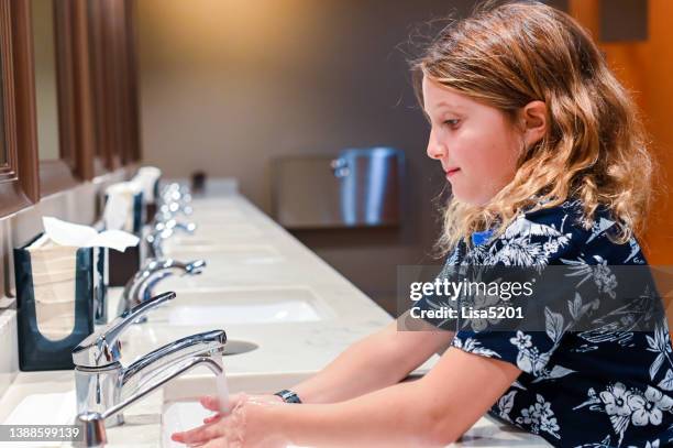 elementary age girl washes her hands at the sink in a public bathroom - public toilet stock pictures, royalty-free photos & images