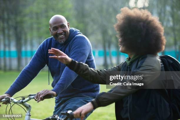 happy father and teen son riding bikes in park - adult riding bike through park stock pictures, royalty-free photos & images