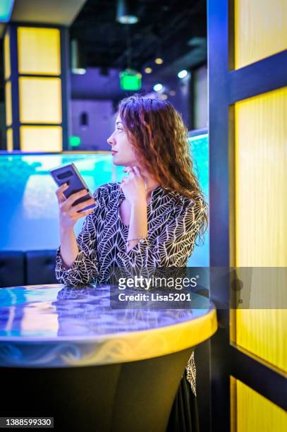 pretty woman in a bar or nightclub uses her cellphone during a night out maybe waiting for friends or bored - dating stockfoto's en -beelden