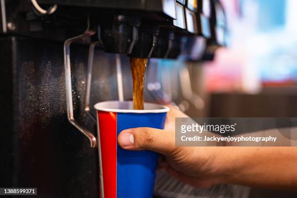 holding a cup at soft drink self service machine pouring cola fizzy drink at a restaurant. - fizz photos et images de collection