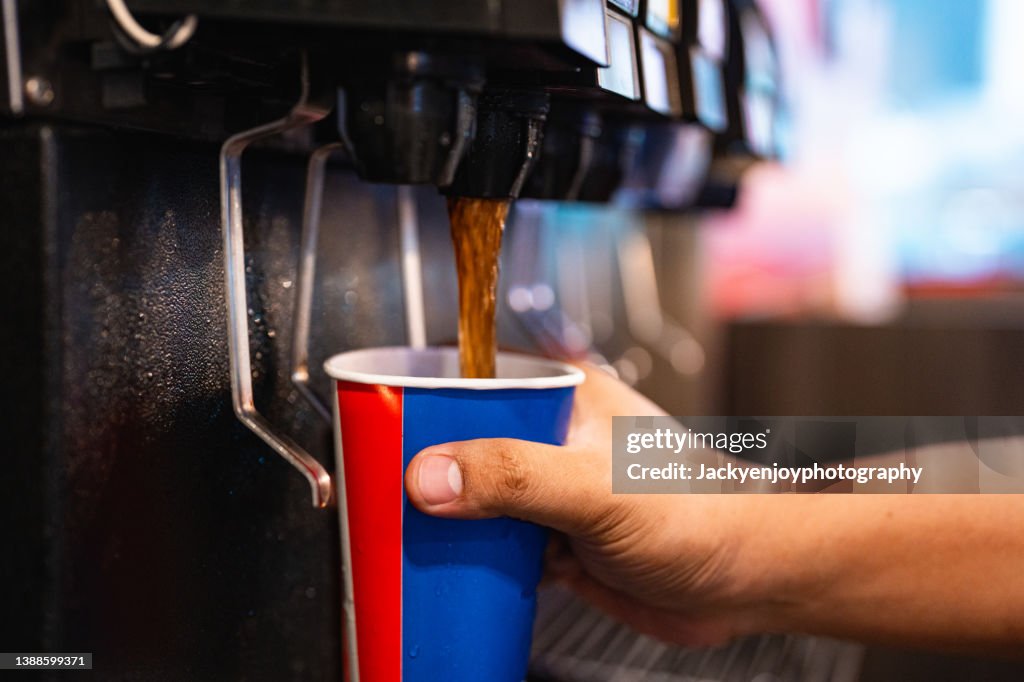 Holding a cup at soft drink self service machine pouring cola fizzy drink at a restaurant.
