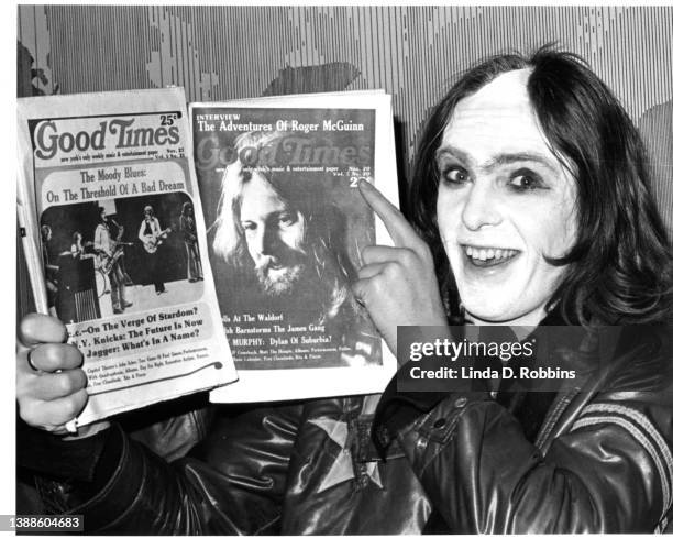 Wearing face paint and a distinctive part-shaved haircut, English singer Peter Gabriel of Genesis holds up November copies of Good Times, the New...