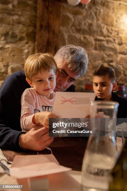 little girl sitting in her grandfather lap reading a letter of congratulations at her baptism celebration - baptism party stock pictures, royalty-free photos & images