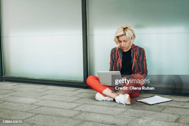 young woman working on laptop sitting cross-legged. - red tile stock pictures, royalty-free photos & images